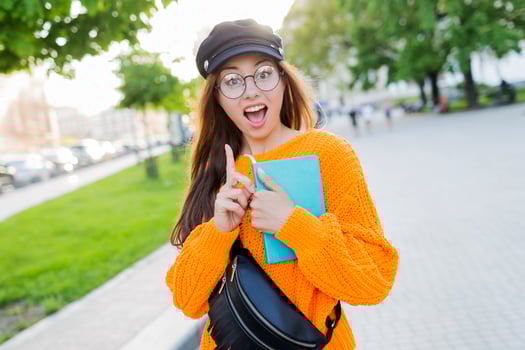 Close-up portrait of shocked charming young woman  pointing with finger, looking at camera with open mouth, holding books. photo