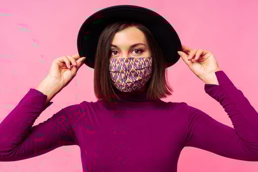 Beautiful woman wearing stylish protective face mask. Pink background. Black hat. Studio photo. photo