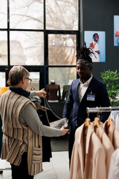 Senior customer discussing black bag material with worker, shopping for casual wear in modern boutique. Elderly client buying fashionable clothes and stylish accessories in clothing store photo