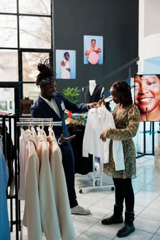 Pregnant woman shopping for maternity clothes in modern boutique, worker helping client with the right shirt. African american customer buying fashionable merchandise in clothing store photo
