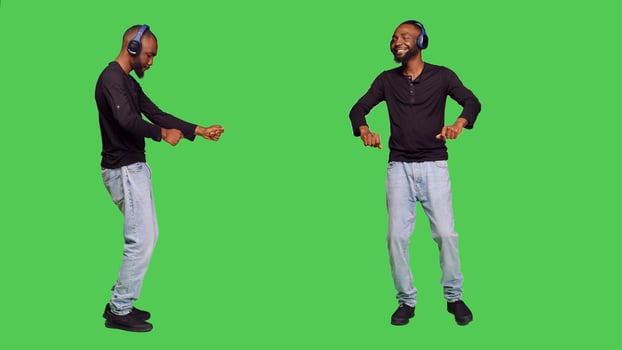 Male model with headphones dancing on camera, listening to music on audio headset and having fun. Young person doing dance moves while he enjoys positive songs, standing over greenscreen. photo