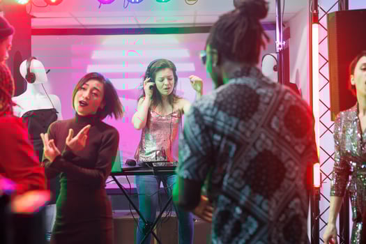 Woman dj in headphones performing using electronic music mixing station on stage while crowd dancing in nightclub. People partying on dancefloor and clubbing at discotheque photo