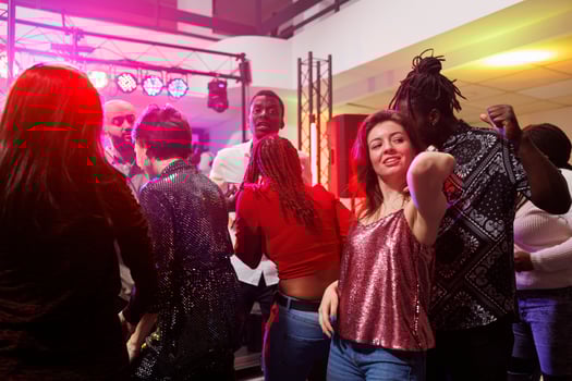 Multiracial couple dancing together while partying in crowded nightclub. Man and woman clubbing and having fun on dancefloor illuminated with spotlights at club discotheque photo