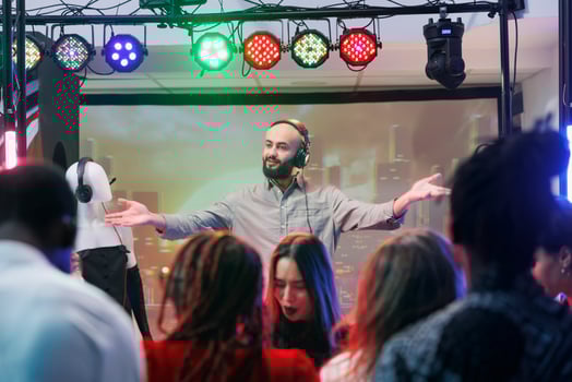 Man dj in headphones performing on nightclub stage at electronic music festival while people dancing. Young musician mixing tracks while clubbers crowd having fun on dancefloor photo