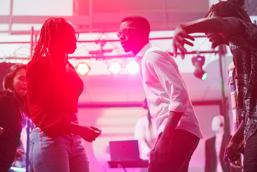 Couple showing improvised dance performance in nightclub illuminated with vibrant lights. Young african american man and woman partying together on dancefloor in dark club photo