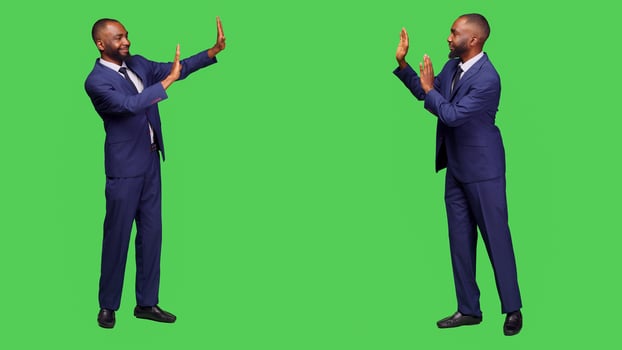 African american employee pushing something aside, showing rejection for an object to left or right sides of studio. Male startup entrepreneur refusing thing over green screen backdrop. photo