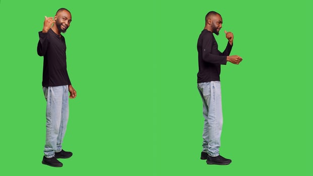 African american person asking someone to come over, posing with jeans and shirt over green screen backdrop. Male model standing in studio and calling someone over to accompany or join. photo