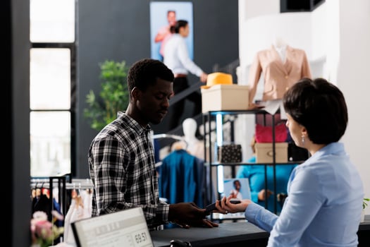 Client using credit card to pay for fashionable clothes during fashion shopping session in modern boutique. African american man buying formal wear using payment terminal in retail store photo