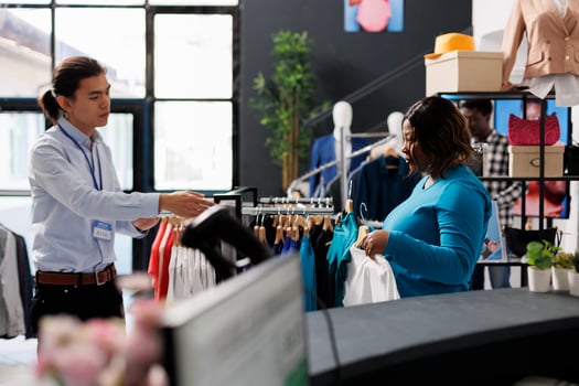 Asian employee discussing with stylish client, showing trendy clothes in modern boutique. African american customer shopping for casual wear, looking at stylish merchandise in clothing store photo