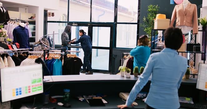 African american robber shoplifting stylish clothes, running from shopping centre. Asian bodyguard catches thief at store door, threatens him with the police in modern boutique. Burglary concept photo