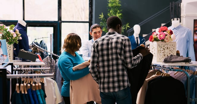 Asian manager helping customers with outfits, explaining clothes fabric in shopping store. African american couple buying fashionable outfit and stylish accessories in modern boutique. Fashion concept photo