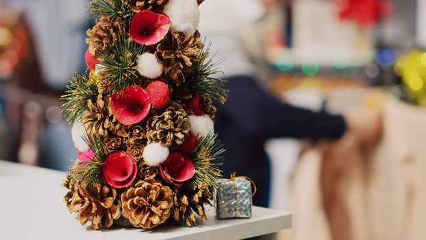 Extreme close up shot of festive miniature Christmas tree adorned with pine cones and flowers sitting on clothing store counter during winter holiday season. Xmas decor in fashion boutique photo
