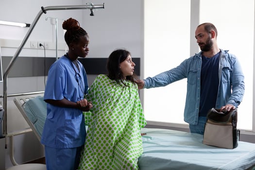 African american obstetrics nurse helping pregnant woman to get out of bed in hospital ward, preparing patient for caesarean surgery. Future parents expecting child in maternity clinic photo
