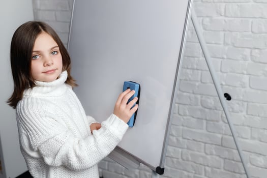 Little girl standing and cleaning whiteboard. Child smiling and looking at camera photo
