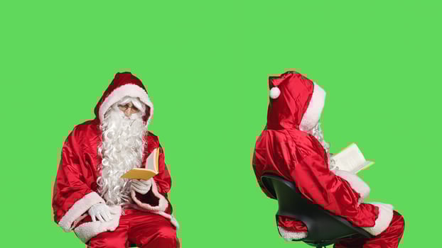Wise person reading for knowledge, enjoying novel story or fairytale while he sits over greenscreen. Man portraying father christmas reads fiction or poetry, sitting on chair. photo