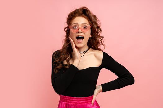 Woman  in suglasses  with suprise face posing over pink background. Wavy hairs. Perfect smile.  Isolate in studio. photo