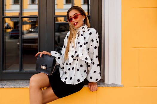 Street fashion look. Graceful blond lady in   White blouse and black skirt standing on yellow background photo