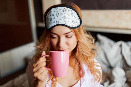 Pretty woman with candid smile posing in eye mask  at home and drinking hot tea. Cozy home atmosphere. photo