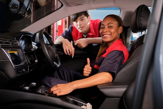 Young Black female automotive mechanic technician and partner check maintenance list in car interior at garage with smiles. Vehicle service fix and repair works, industrial occupation business jobs. photo