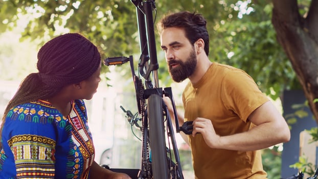 Dedicated multiracial pair cautiously fastening bike chain and pedal for summer outdoor leisure cycling. Outdoorsy young couple thoroughly examining damages on bicycle wheel for repairing. photo