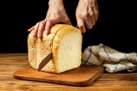 Female hands cutting fresh white homemade bread on a wooden board on a wooden table. Homemade cakes, pastries. photo