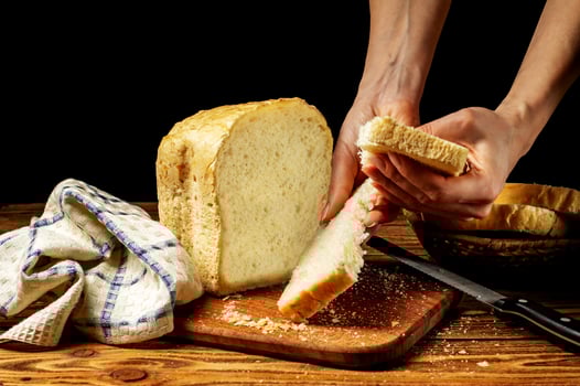 Female hands breaking a piece of fresh white homemade bread that stands on a wooden table. Homemade cakes, pastries. photo