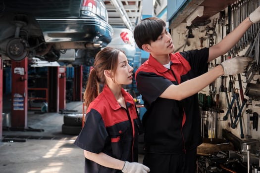 Two professional Asian mechanic partners discuss hand tools and machinery for fixing work at car service garage, maintenance jobs, and check and repair occupation in automotive industry business. photo