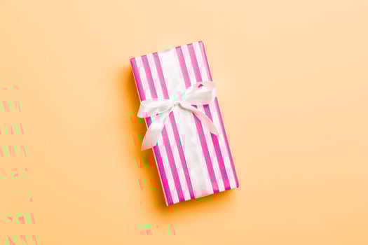 wrapped Christmas or other holiday handmade present in paper with white ribbon on orange background. Present box, decoration of gift on colored table, top view with copy space photo