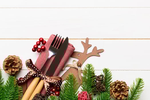 Top view of holiday objects on wooden background. Utensils tied up with ribbon on napkin. Christmas decorations and reindeer with copy space. New year dinner concept photo