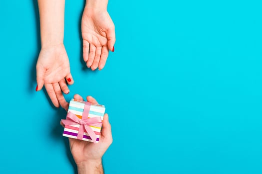 Top view of a man holding and giving a gift to a woman on colorful background. Receiving a present. Close up of holiday concept photo