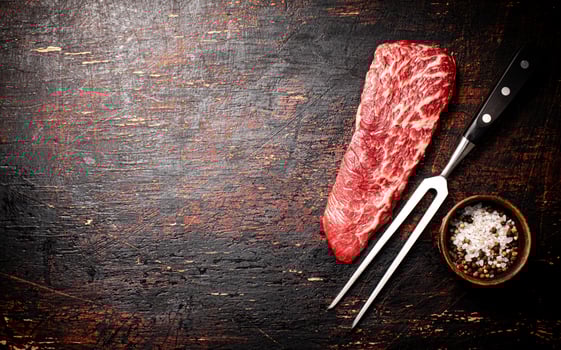 Raw steak with a large fork on the table. photo