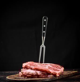 Raw pork steak on a cutting board with fork. photo
