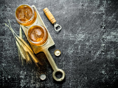 Two glasses of beer on a stand with spikelets and opener. photo