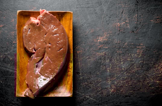 Piece of raw liver on a wooden plate. photo