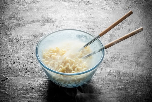 Heated instant noodles in glass bowl with chopsticks. photo