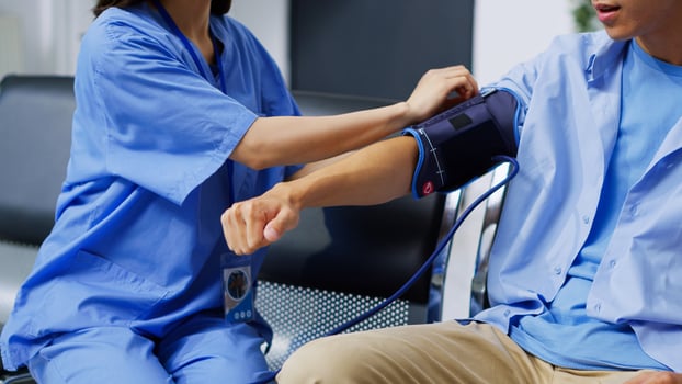 Asian nurse checking patient hypertension using medical tonometer during checkup visit appointment in hospital waiting area. Assistant examining elderly man blood pressure in reception photo