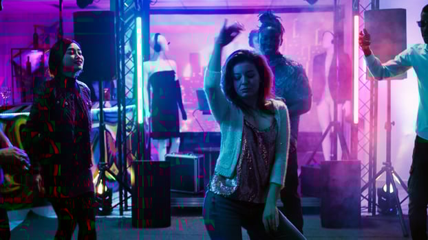Group of friends having fun at club, partying and jumping around in discotheque. Young funky people enjoying nightlife with electronic music on stage, dancing at nightclub. Handheld shot. photo