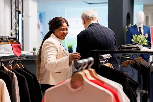 Friendly smiling black woman shop assistant helping senior man customer to choose clothes in fashion boutique. Helpful pleasant African American saleswoman serving assisting shopper in clothing store photo
