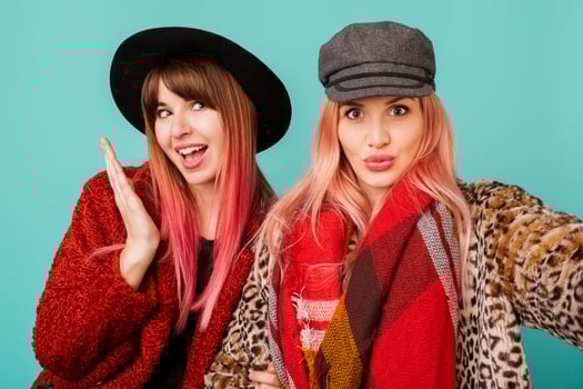 Close up studio portrait of two pretty cute models with pink hairs in stylish leopard print faux fur coat and trendy hat on turquoise. Surprise face. Winter fashionable outfit. photo