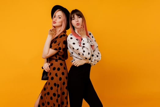Couple of  lovely  women, fashionable friends sends kiss to camera and  posing over yellow background. Summer trendy vintage outfit. Shopping and fashion concept. photo