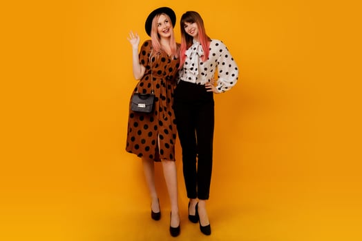 Full-length Studio image of stylish  females in dress posing over yellow background. Glad female models in stylish clothes. Shopping and fashion concept. photo