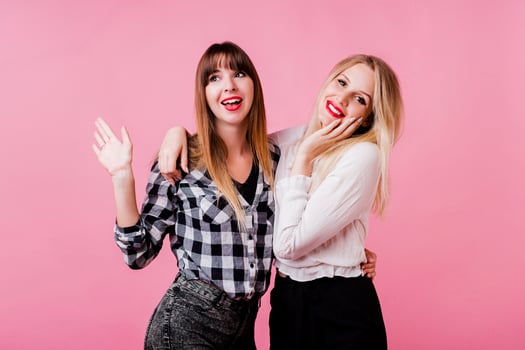 Two smiling women hugging and standing isolate over pink background . Brunette and blonde girls. Natural make up. photo
