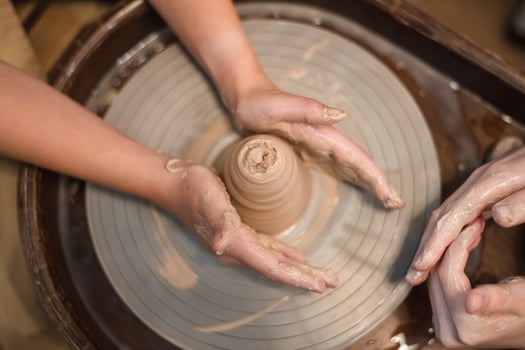 Potter girl works on potter's wheel, making ceramic pot out of clay in pottery workshop photo