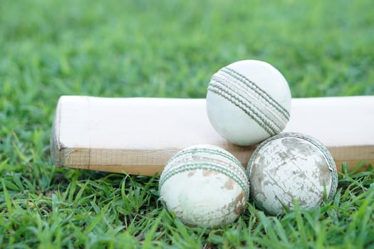 White cricket ball on wooden bat. Concept, sport equipment. Competitive sport. A cricket ball is made with a core of cork, covered by a leather case with a slightly raised sewn seam photo