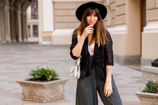 Street fashion photo of stylish brunette woman in casual outfit  and black hat. Enjoing vacation in european city.