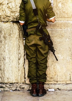 Back of unidentifiable Israeli solder praying on Wailing Western Wall in Jerusalem, Israel with his M16 automatic weapon to his side photo