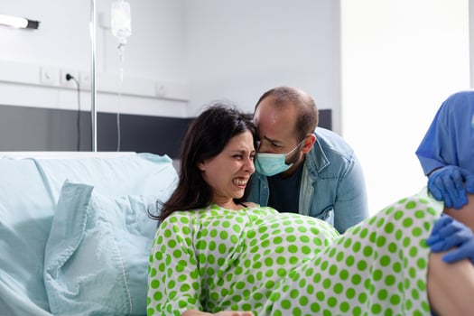 Diverse medical team helping woman with pregnancy to delivery baby in hospital ward. Pregnant patient having painful contractions being comforting by husband while giving birth to child photo