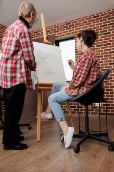 Adult daughter and senior mother doing art together while attending drawing workshop, learning to draw, developing common interests and hobbies. Teacher and student looking at canvas with artwork photo