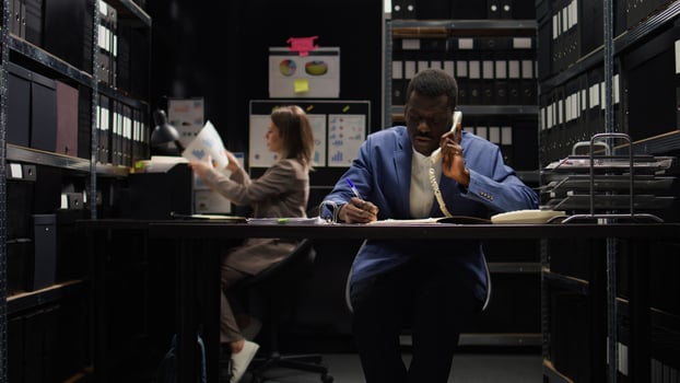 In police department office, detective answers phone, obtaining new case information and forensic evidence report to catch suspect. Private investigator is speaking on the phone with a criminologist. photo