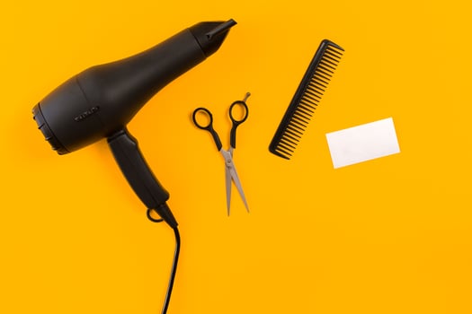 Black hair dryer, comb and scissors on yellow paper background. Top view photo